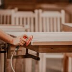 Amish craftsman sanding the edge of a solid wood dining table in the workshop
