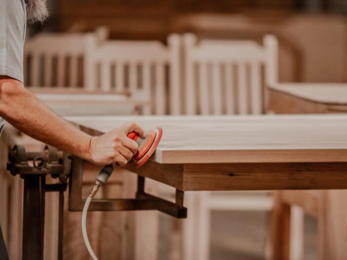 Amish craftsman sanding the edge of a solid wood dining table in the workshop